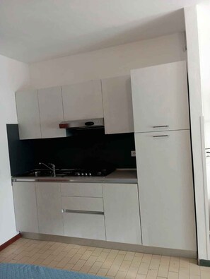 A compact kitchen with white cabinets, a stove, and a sink.