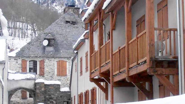Ein traditionelles Steinhaus mit hölzernen Balkonen und einem schneebedeckten Berg im Hintergrund.