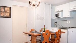 Ein Essbereich mit Holztisch und Stühlen, einer Pendelleuchte, einer weißen Tür und einer Küche mit Mikrowelle und Kühlschrank.