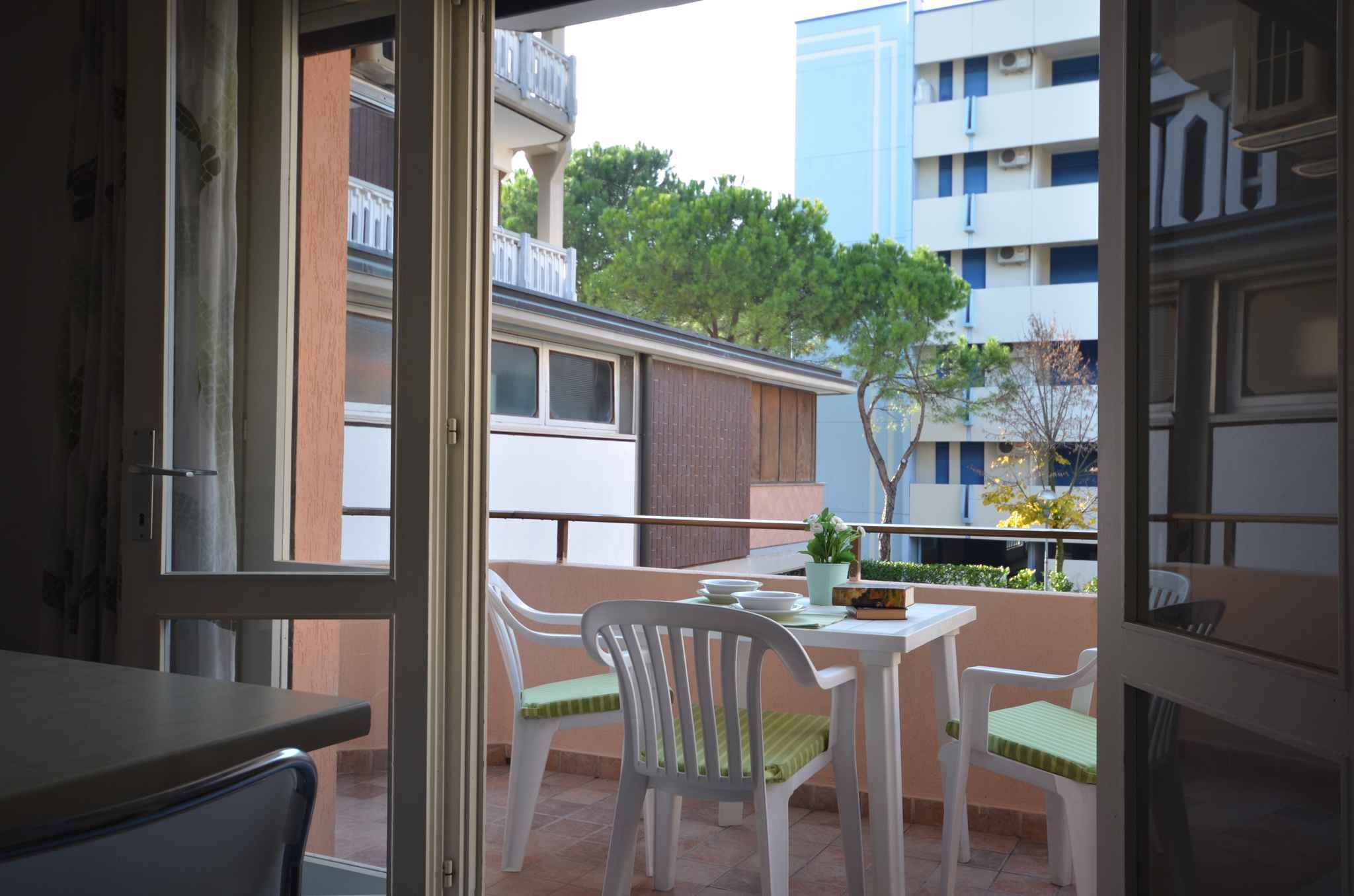 Een balkon met een tafel en stoelen, een plant in een pot en uitzicht op een gebouw en bomen.