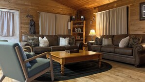 Un acogedor interior de cabaña de madera con un conjunto de sofás, una mesa de centro de madera y una estantería.