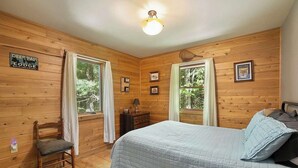 Una habitación con paneles de madera, una cama, una silla y dos ventanas.