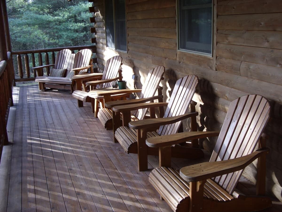 A wooden deck with Adirondack chairs and a table, overlooking a forested area.