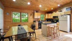 Interior de una cabaña de madera con cocina, mesa de comedor y taburetes de bar.