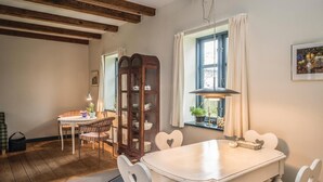 Uma sala de jantar com mesa e cadeiras brancas, um armário de madeira e uma janela com cortinas.