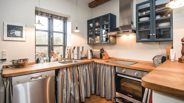 Cozinha moderna com máquina de lavar louça, forno e cortinas listradas.