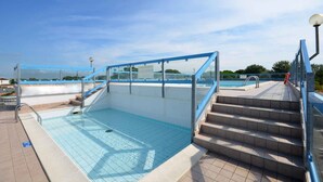 Una piscina exterior con cerramiento de cristal, escalones que bajan al agua y un cielo despejado al fondo.