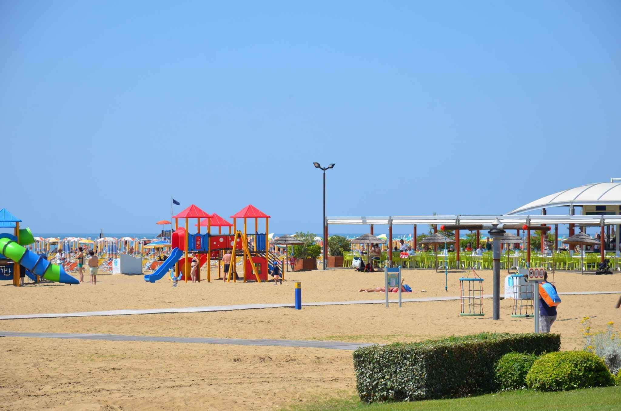 A beachside playground with slides and play structures, a covered seating area, and a clear sky.