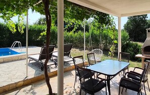 Een terras buiten met een zwembad, stoelen, een tafel en een barbecue.