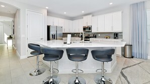 A modern kitchen with white cabinets, a central island with bar stools, stainless steel appliances, and a tiled backsplash. - Modern Home near Disney: Media, Game & Themed Rooms + Waterpark - 384SF (Kissimmee)