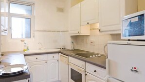 Eine Küche mit weißen Schränken, einem Herd, einem Kühlschrank und einem Fenster.