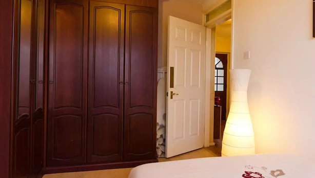 Ein Schlafzimmer mit einem hölzernen Kleiderschrank, einer weißen Tür, einer Nachttischlampe und einem Bett mit floralem Bettbezug.