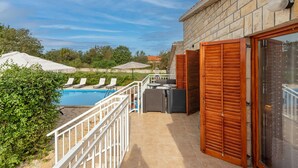 Un espace aménagé au bord de la piscine, avec un mur en pierre, une porte en bois et une vue sur la piscine.