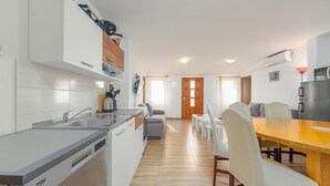 Une cuisine moderne équipée d’un lave-vaisselle, un coin repas avec une table et des chaises en bois, et un espace de détente avec un canapé et une machine à café.