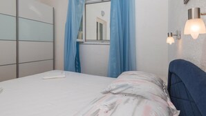 Un dormitorio con cama, armario, ventana con cortinas y una lámpara fijada a la pared.