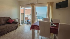 Una habitación con sofá, una mesa de comedor con sillas, un televisor montado en la pared y un balcón con vistas al mar.