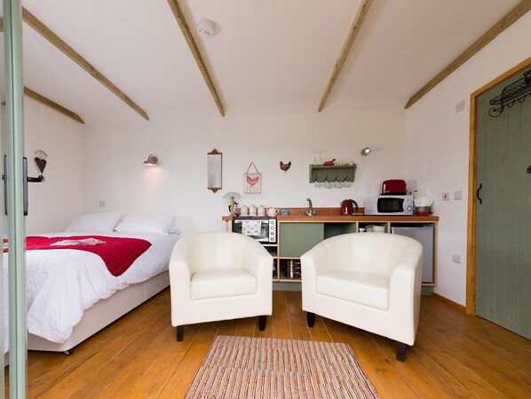 A bedroom with a bed, two white armchairs, a small kitchenette, and a wooden ceiling. - 1 bedroom accommodation in Wootton Bridge (Wootton Bridge)