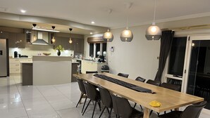 A modern kitchen with a central island, a dining area with a long wooden table and chairs, and pendant lighting. - In the Hunter Valley and need a place to stay for a big group? Look no further (Bellbird)