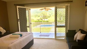A bedroom with a bed, a sofa, and a view of a pool and greenery through a sliding door. - In the Hunter Valley and need a place to stay for a big group? Look no further (Bellbird)