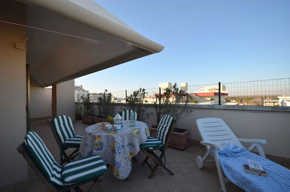 A balcony with a table and chairs, a lounge chair, and potted plants.