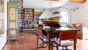 Een ruime kamer met een groot houten bureau, een piano en een boekenkast vol boeken.