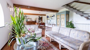 Een woonkamer met een gestreept bankje, een salontafel met planten, een houten kast met decoratieve objecten, en een trap.