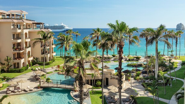 A resort with a pool area, palm trees, and a view of the ocean.