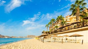A beach resort with a sandy shoreline, palm trees, and a mountain in the background.