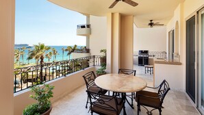 A balcony with a round table and chairs, a ceiling fan, and a view of the beach.