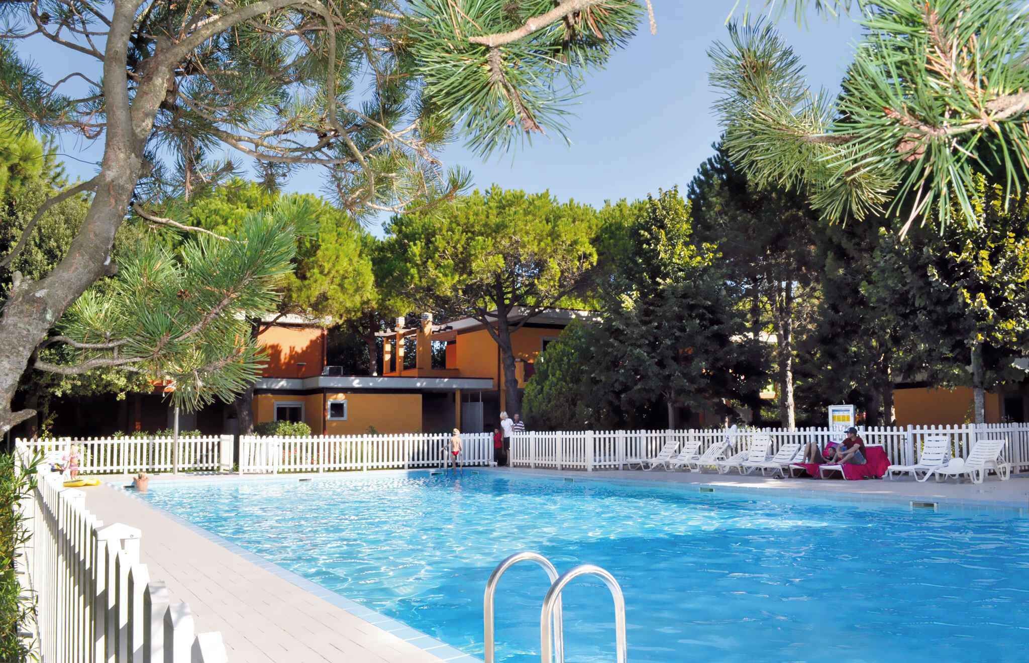 A swimming pool with a white fence, surrounded by trees and a building with a white picket fence.