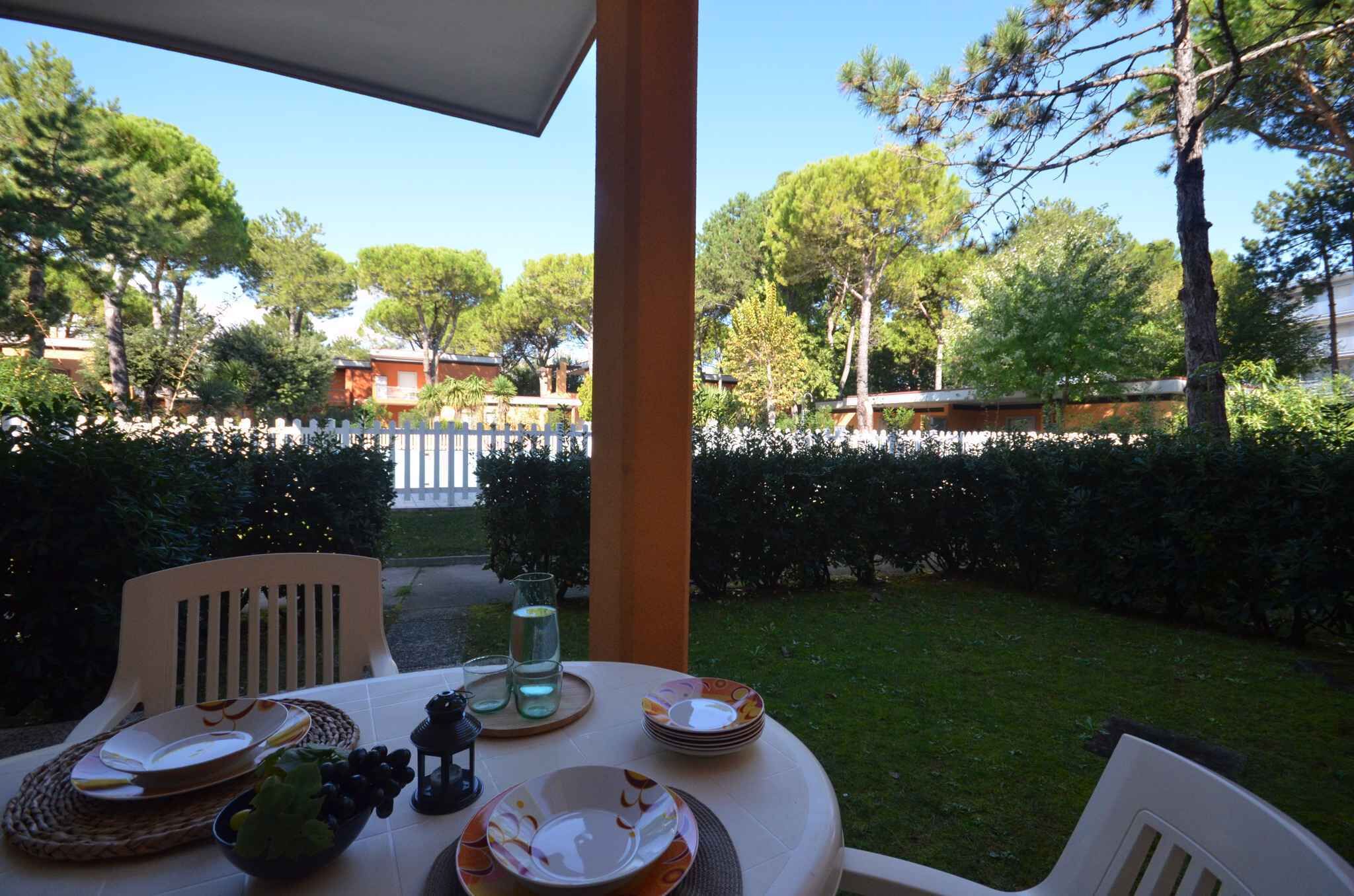 Un espace extérieur aménagé pour prendre les repas, avec une table dressée pour deux personnes, entouré de verdure et délimité par une clôture blanche.