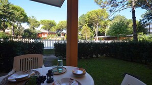 Un espacio de comedor al aire libre con una mesa dispuesta para dos personas, rodeado de follaje y una valla blanca.