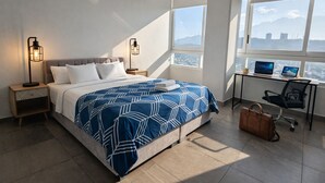Une chambre d’hôtel moderne avec un grand lit, deux lampes de chevet, un bureau avec un ordinateur portable et une vue sur le paysage urbain.
