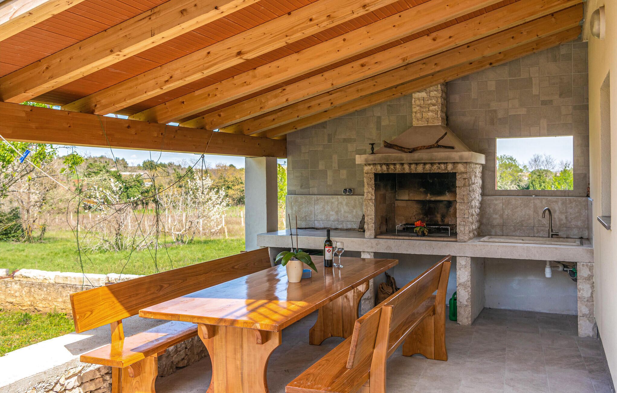 Eine Außenküche mit Kamin aus Stein, Holzbanken und einem Tisch.