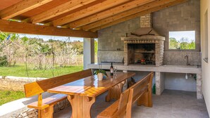 Une cuisine extérieure dotée d’une cheminée en pierre, de bancs en bois et d’une table.