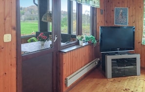 Une pièce aux murs en bois, avec une grande fenêtre, un téléviseur et un radiateur.