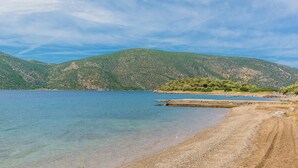 A beach with clear water, a dirt path, and green hills in the background. - Seafront Holiday Villa (Skroponeria Politeia)