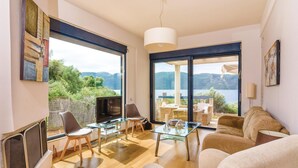 A modern living room with a TV, glass coffee table, and seating area. - Seafront Holiday Villa (Skroponeria Politeia)
