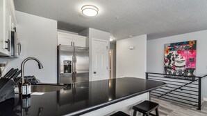 A modern kitchen with a stainless steel refrigerator, a black countertop, and a bar stool. - Stay cool with great rates and central Air conditioning! Weber County lic #3495 (Eden)