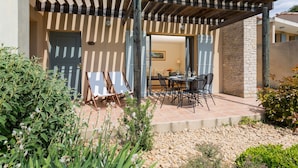 Un porche cubierto con un muro de piedra, mobiliario exterior y vista hacia el interior de la casa.