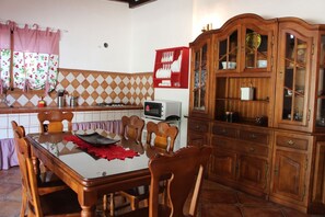 Uma área de refeições com mesa, cadeiras, micro-ondas e um armário de madeira com portas de vidro.
