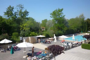 Un espace aménagé au bord de la piscine, avec des chaises longues et des parasols, le tout entouré de verdure.