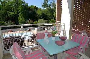 Un balcon avec vue sur la piscine, un espace salon extérieur et une table avec des bols et une plante.