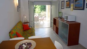 Ein kompakter Wohnbereich mit Sofa, Esstisch, Fernseher und Schrank.