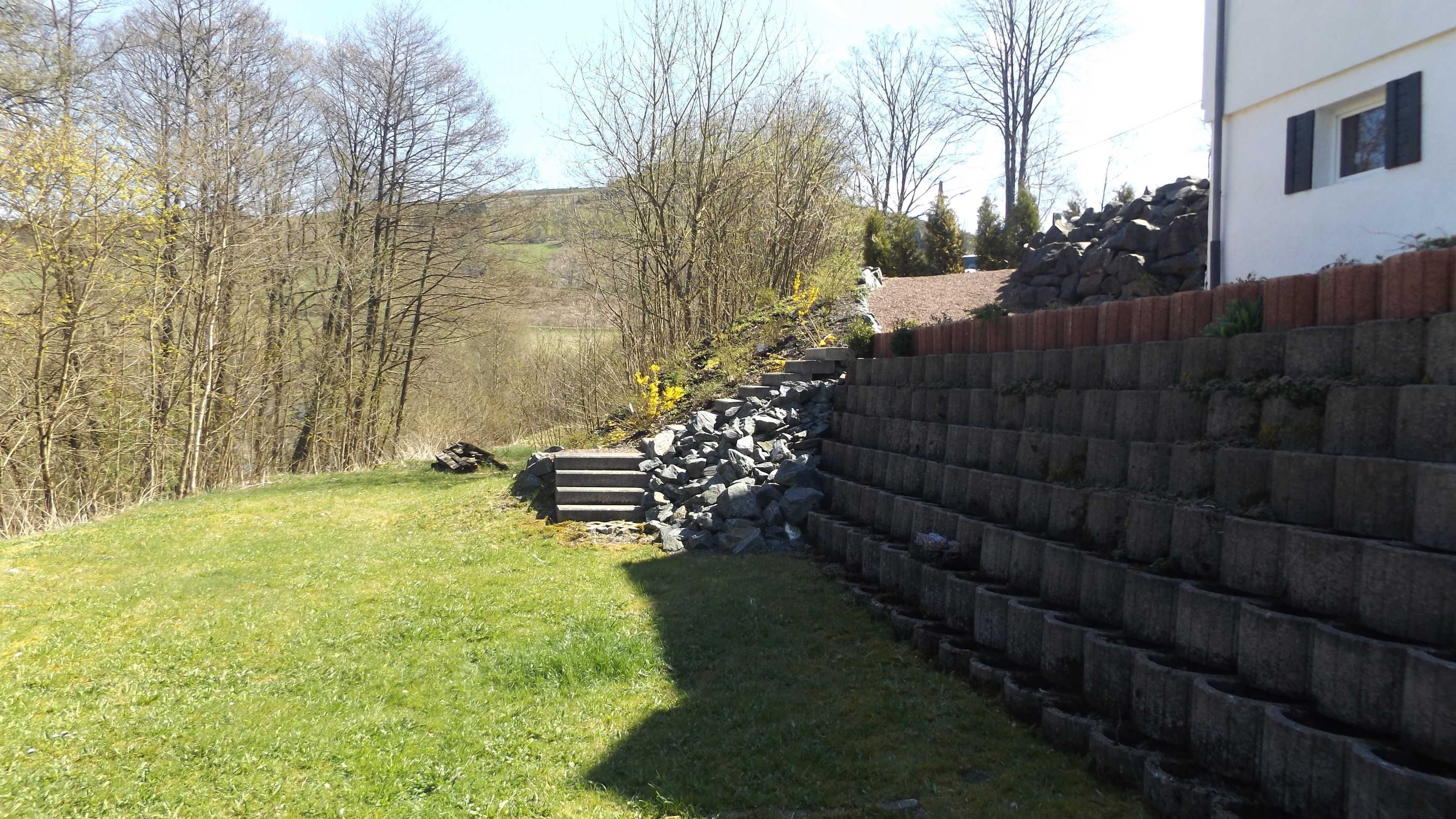 A grassy yard with a stone wall and steps leading up to a building.