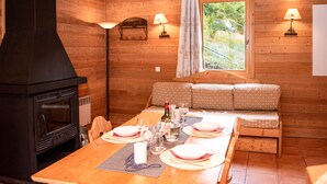 A cozy cabin with a wooden interior, a fireplace, a dining table set for four, and a sofa.