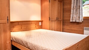 A wooden room with a bed, wardrobe, and a window with curtains.