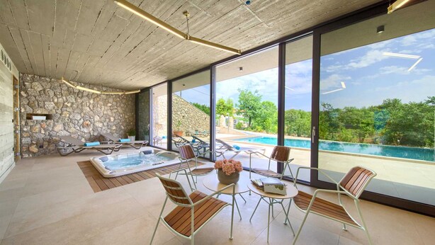 Un espace piscine intérieur moderne, doté d’un mur en pierre, d’un jacuzzi et de chaises longues.