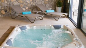 Un bain à remous doté d’un panneau de commande, entouré de chaises longues avec des coussins bleus, le tout adossé à un mur de pierre.