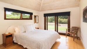 A bedroom with a large bed, a nightstand, a chair, and a view of the outdoors through a sliding door. - Yallingup Retreat - *Romantic, overlooking a lake, secluded* (YALLINGUP)